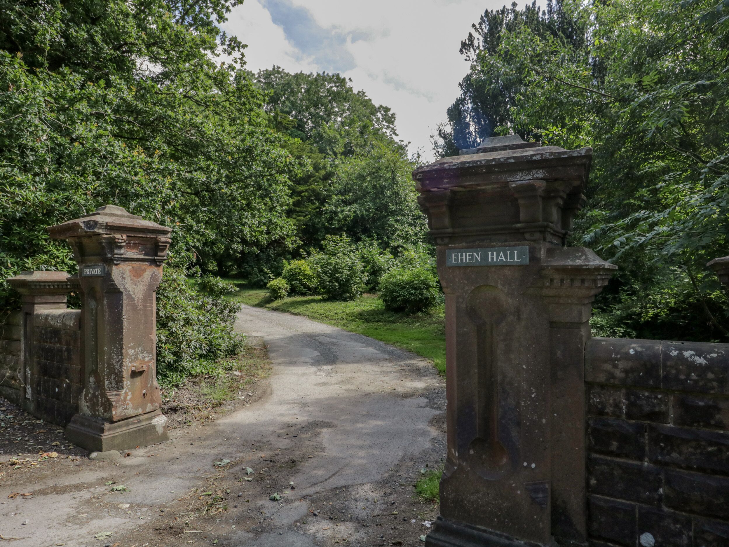 Une porte d’entrée privée, surmontée d’une enseigne indiquant « Ehen Hall », mène à un sentier bordé d’une végétation luxuriante.