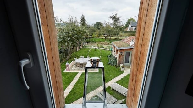 Vista desde una ventana a un patio trasero con césped, una terraza de madera y una casa pequeña.