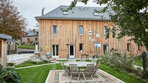 Una casa de madera con un amplio patio, una mesa redonda y mobiliario para exteriores.