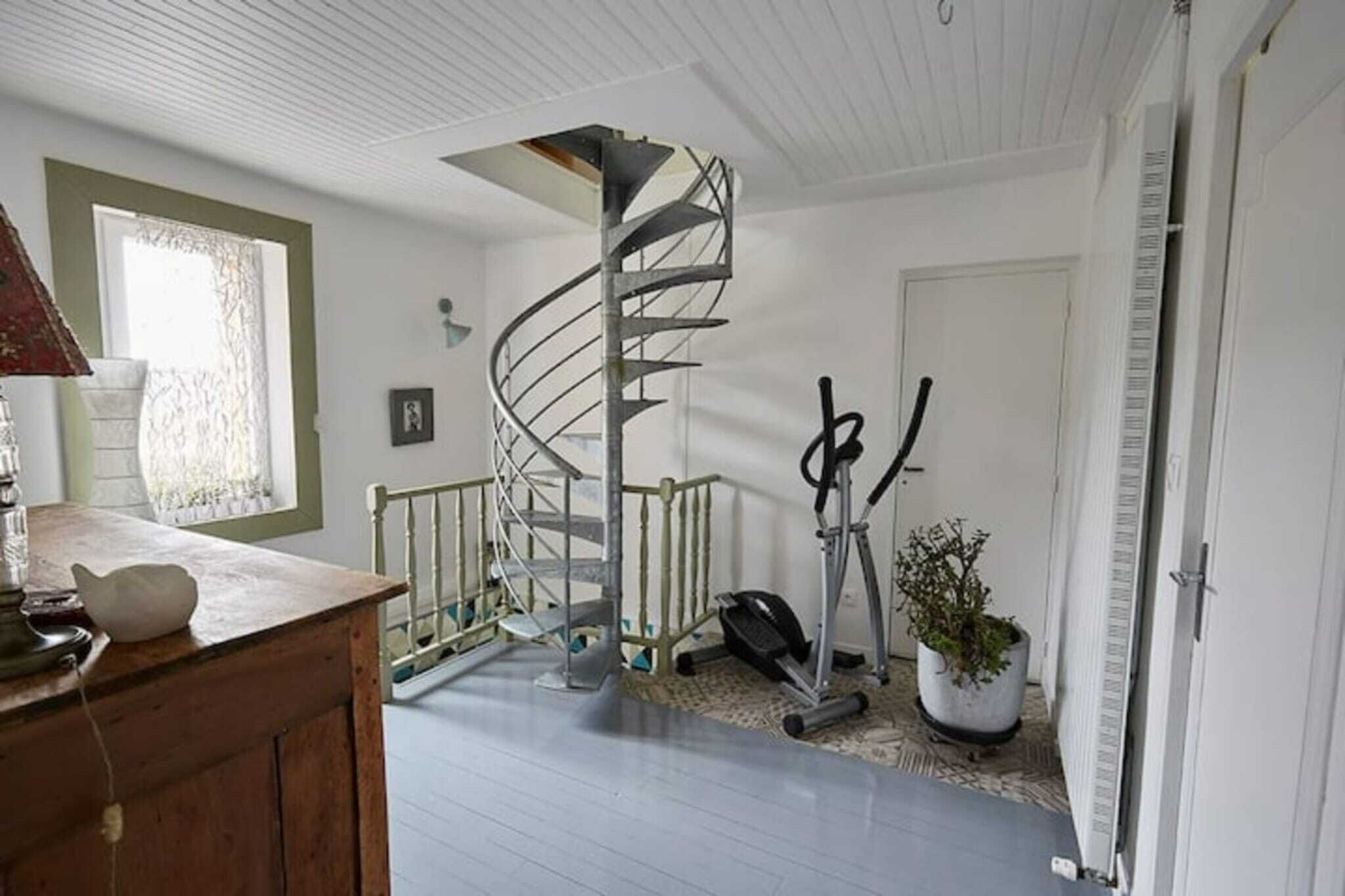 Une pièce dotée d’un escalier en colimaçon, d’appareils de musculation, d’un bureau en bois et d’une plante en pot.