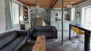Una sala de estar moderna con un sofá de cuero negro, una mesa de centro de madera y una zona de cocina con microondas y estufa.