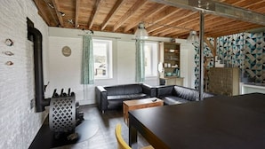 Una sala de estar moderna con un sofá de cuero negro, una mesa de centro de madera y una silla amarilla. Hay una zona de cocina con un salpicadero estampado y un armario.