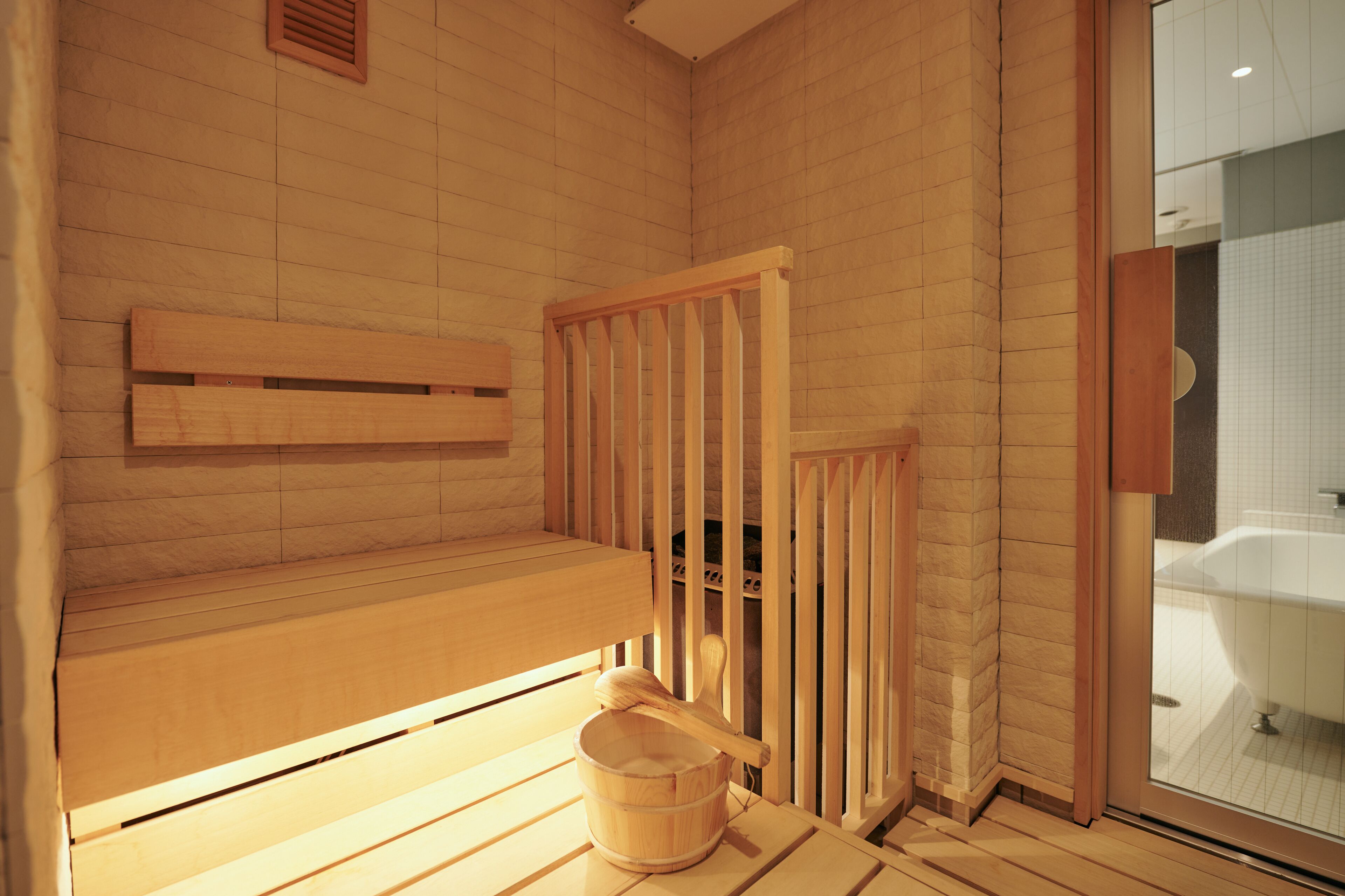Um salão de sauna de madeira com um banco, um balde de madeira e um corrimão de madeira.