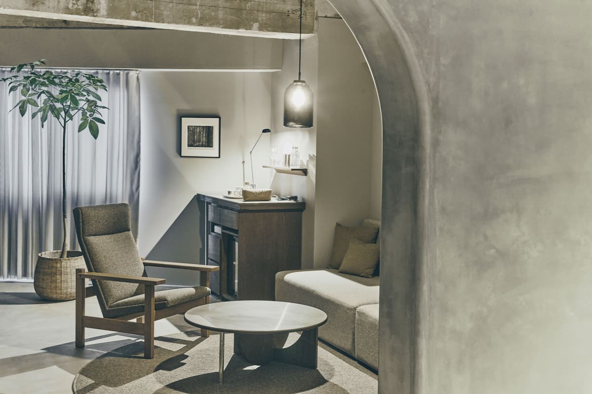 Una sala de estar moderna con un sofá, un sillón y una mesa de centro. Hay un comedor con una mesa y sillas, una lámpara colgante y una planta.