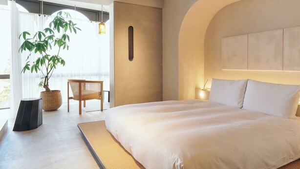 A modern bedroom with a large bed, a potted plant, and a view of the outdoors. - Korinkyo (Kanazawa)