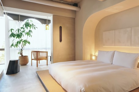 A modern bedroom with a large bed, a potted plant, and a view of the outdoors.