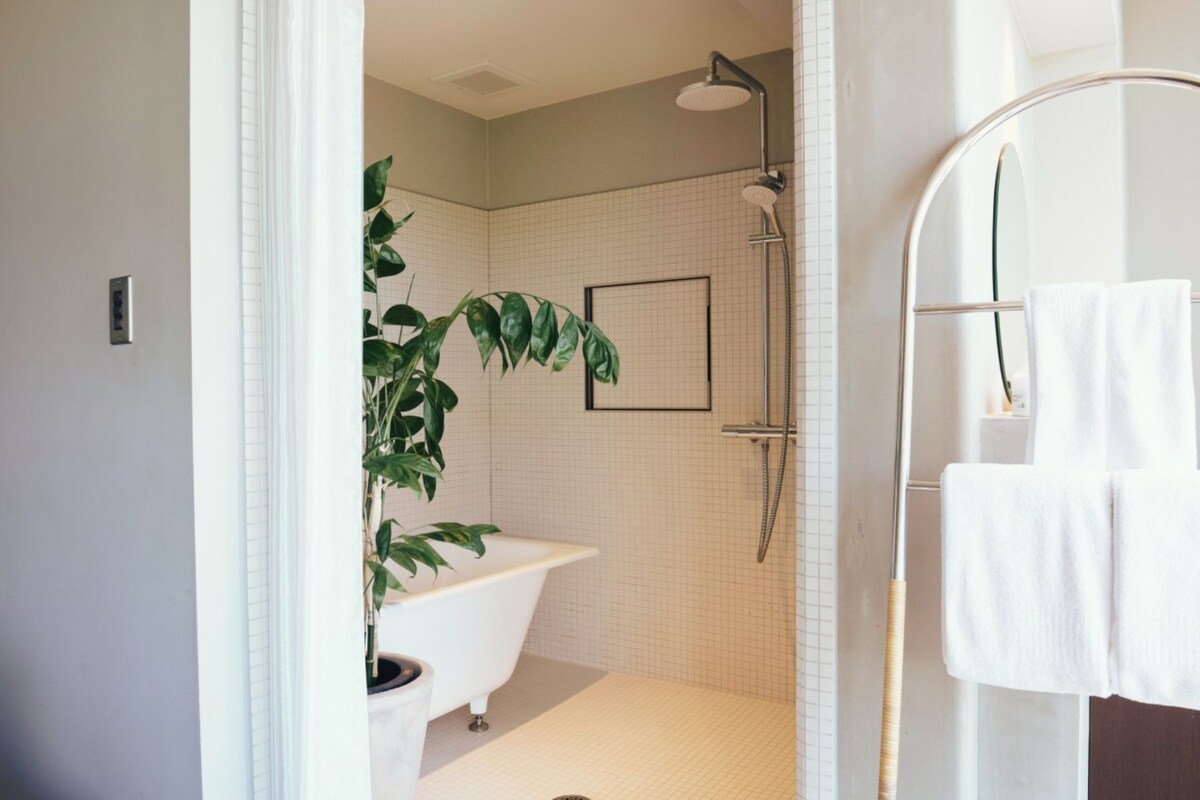 A bathroom with a bathtub, shower, and a potted plant.