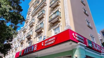 Un edificio de varios pisos con fachada roja y verde, que presenta un letrero con números de contacto.