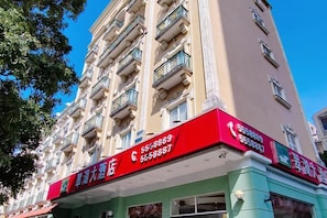 Edifício de vários andares com fachada em vermelho e verde, apresentando uma placa com números de contato.