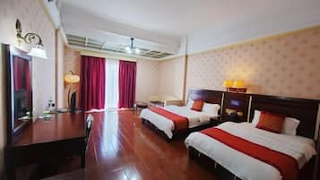 Habitación de hotel con dos camas, un escritorio de madera, una lámpara y un ventanal con cortinas.