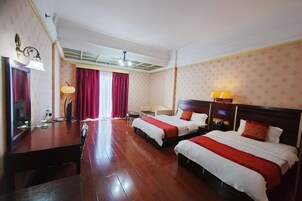 Habitación de hotel con dos camas, un escritorio de madera, una lámpara y un ventanal con cortinas.