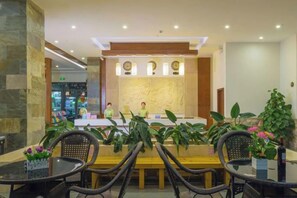 Un hall d’hôtel comprenant un comptoir d’accueil, un espace salon et des plantes en pot.