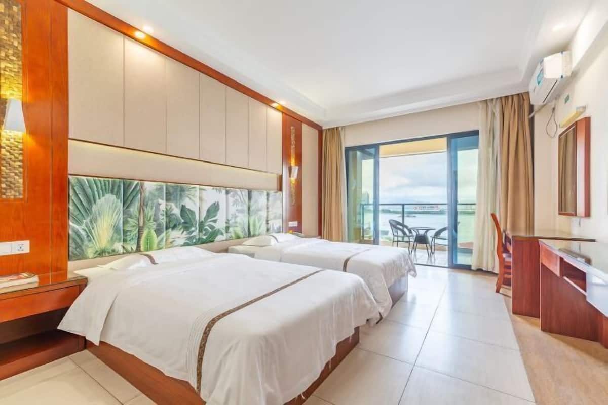 A hotel room with two beds, a large window with a view, a desk, and a chair.