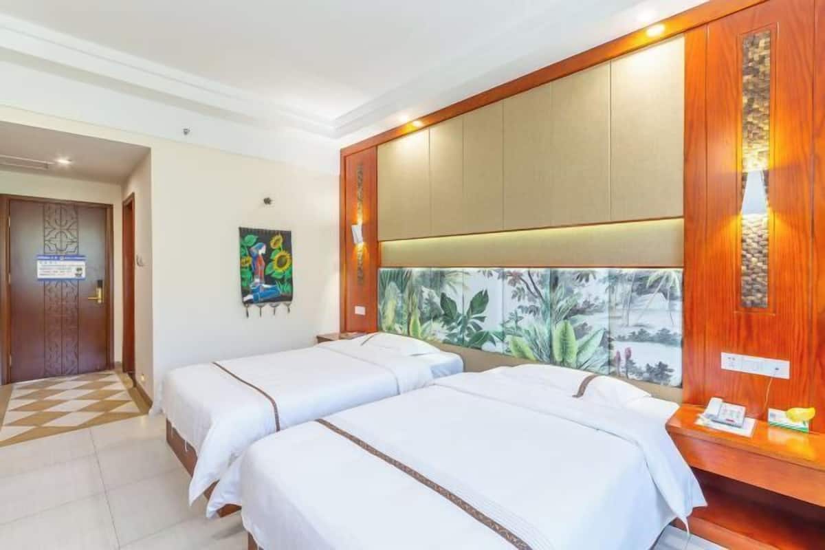 A hotel room with two single beds, a wooden headboard, a small desk with a telephone, and a tropical-themed wall mural.