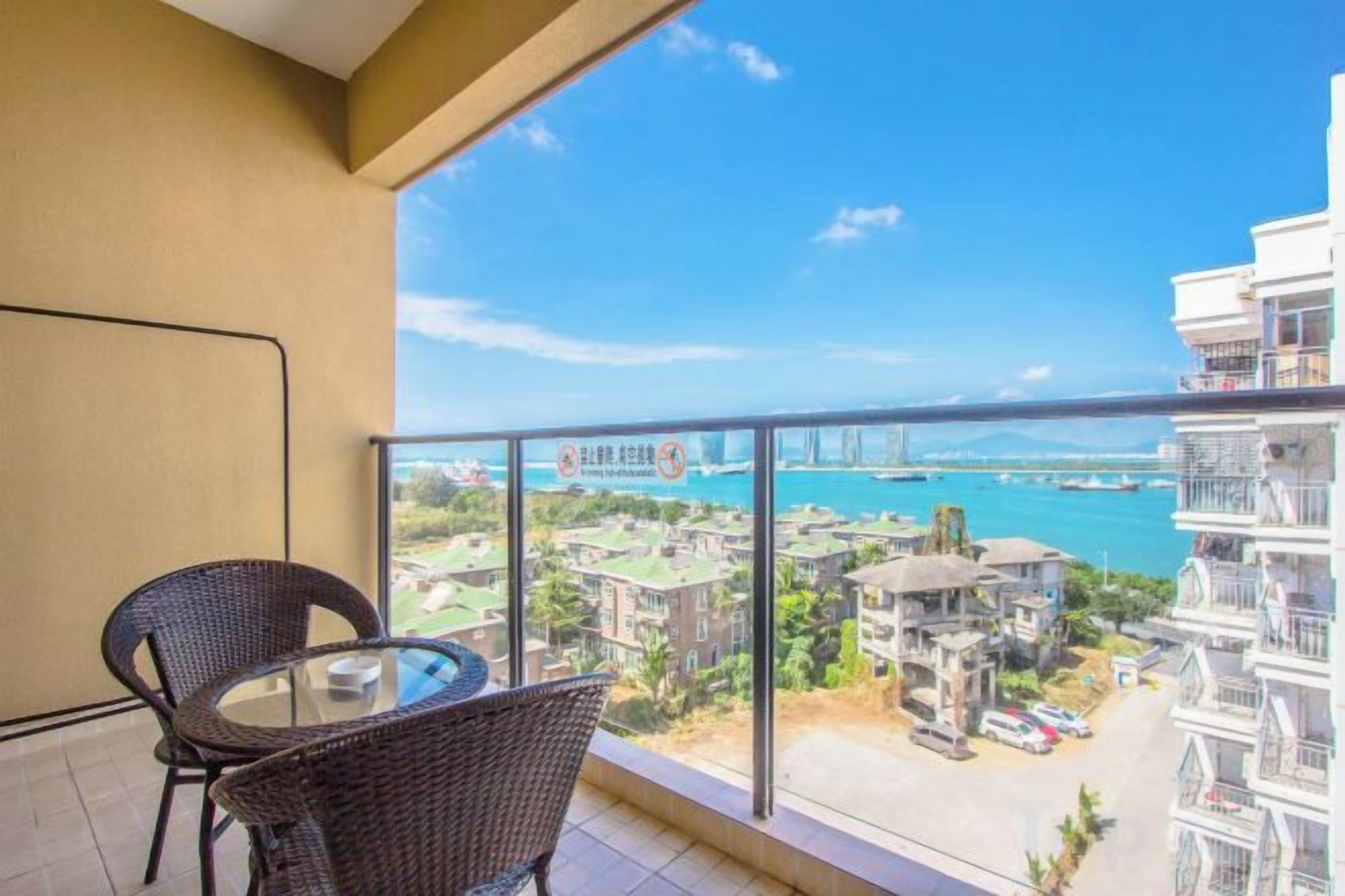 A balcony with a table and chairs, overlooking a coastal area with buildings and a bridge.