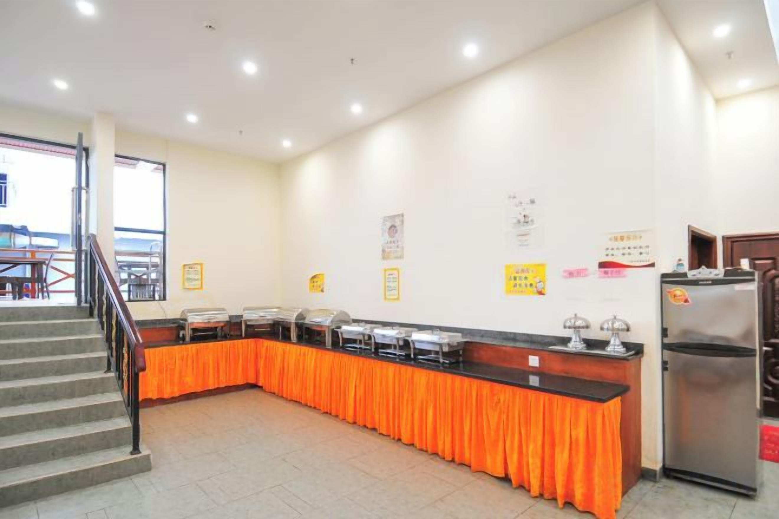 A buffet setup with a counter and a refrigerator, a staircase, and a wall with some notices.
