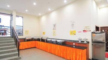 A buffet setup with a counter and a refrigerator, a staircase, and a wall with some notices.