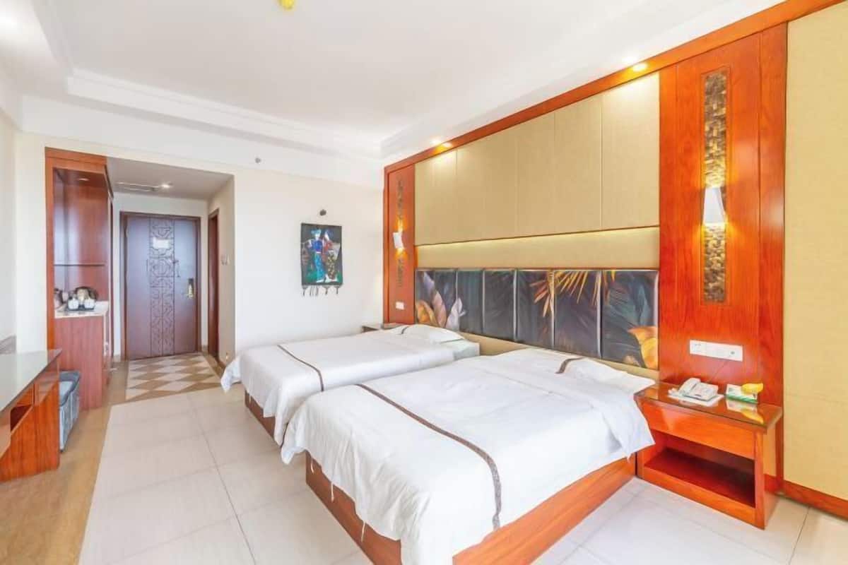 A hotel room with two beds, a wooden headboard, a desk, and a small seating area.