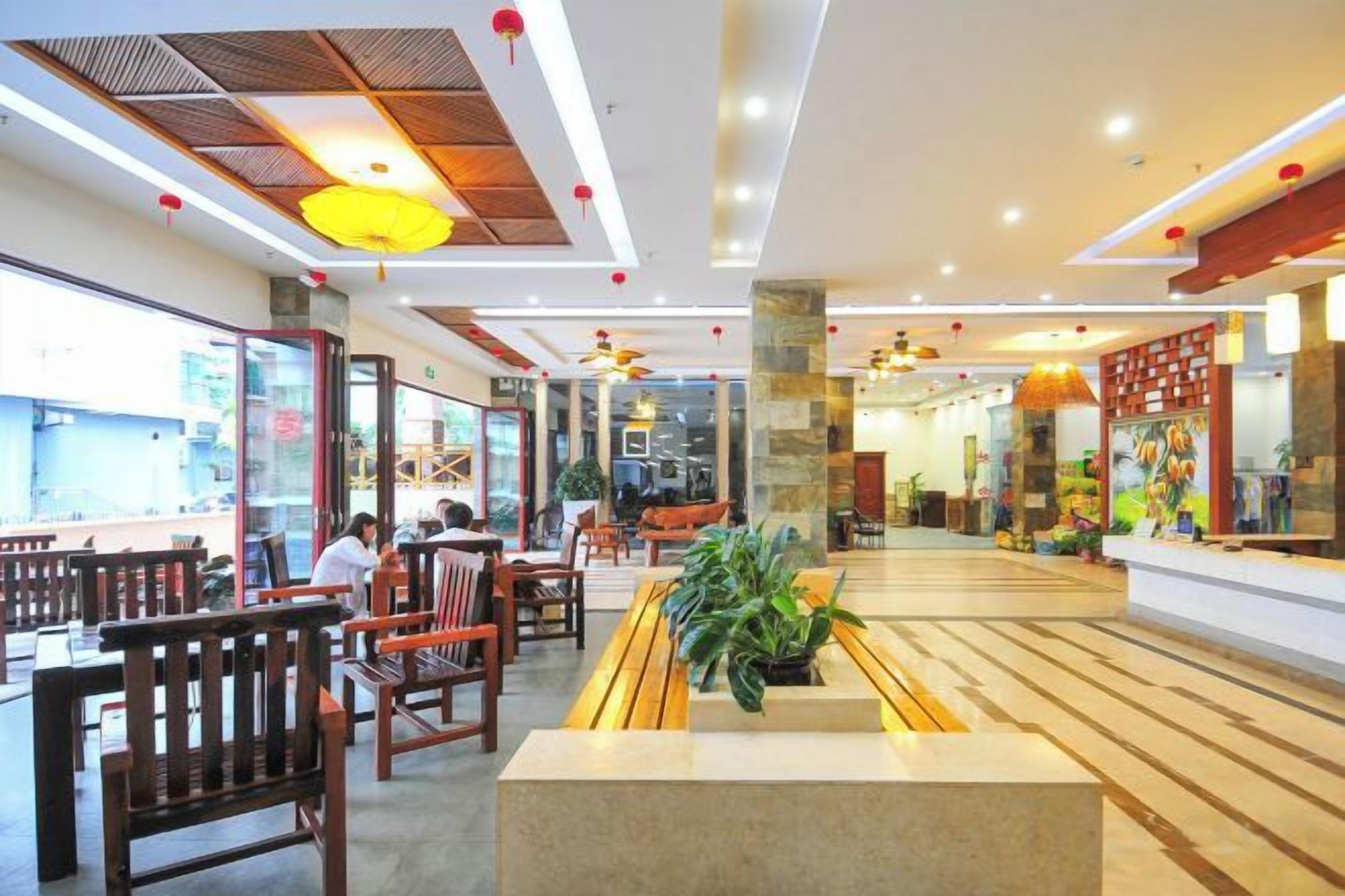 A spacious restaurant with wooden furniture, a central planter with greenery, and a modern ceiling design.