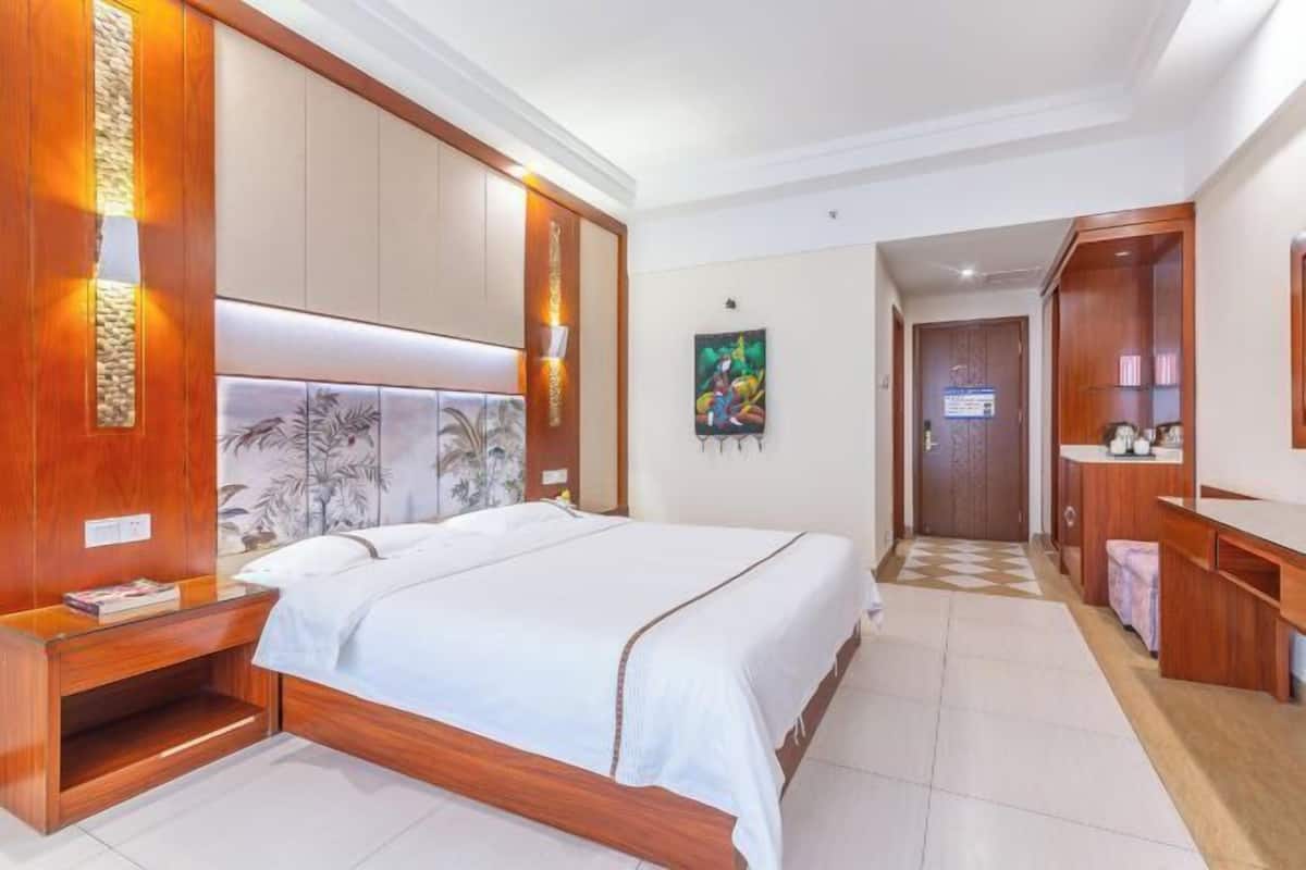 A hotel room with a large bed, wooden headboard, a small bedside table, a wardrobe, and a bathroom visible through an open door.