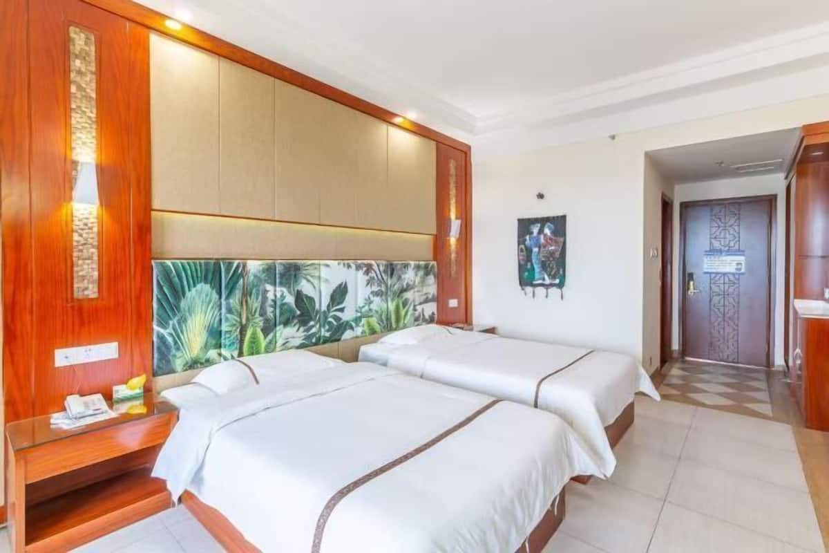 A hotel room with two beds, a wooden headboard, a wall with a tropical mural, and a small desk with a telephone.