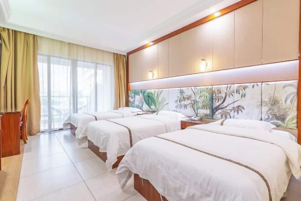 A hotel room with three beds, a desk, and a large window with curtains.