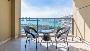 A balcony with two wicker chairs and a glass table, overlooking a coastal area with a bridge and buildings. - Xingyu Sea View Hotel (Sanya Nanbian, Hailu Huitou) (Sanya)