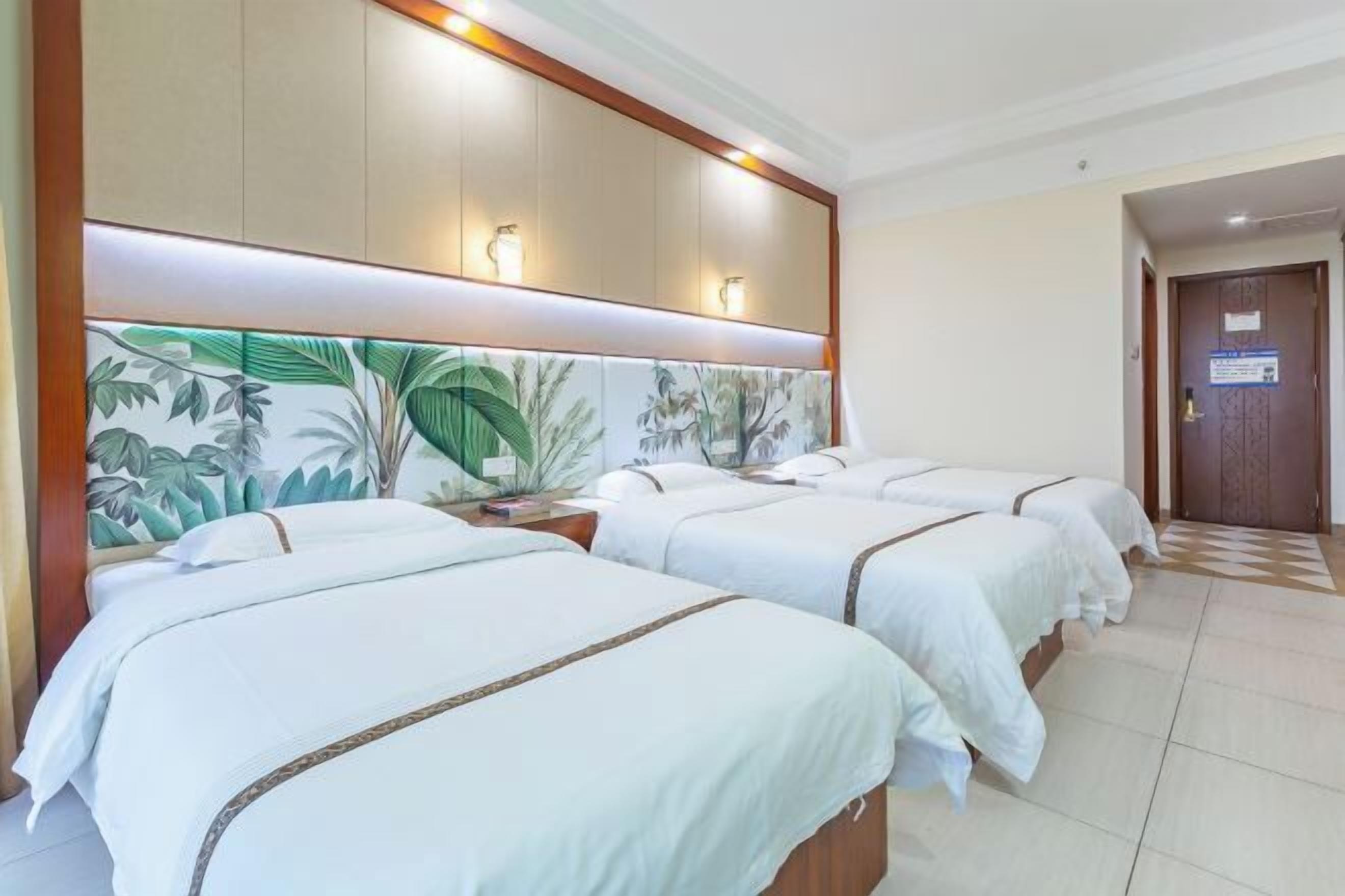 A hotel room with three beds, a large mural with tropical leaves, and a wooden headboard.