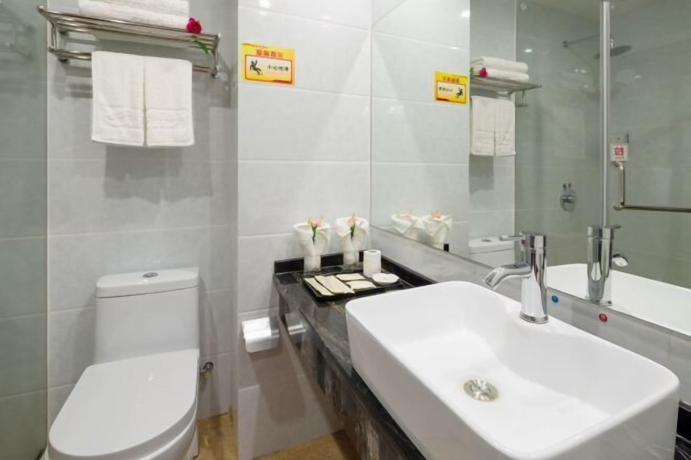Une salle de bain moderne avec un lavabo blanc, un miroir et des toilettes. On y trouve des serviettes et des articles de toilette sur le comptoir.