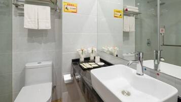 Une salle de bain moderne avec un lavabo blanc, un miroir et des toilettes. On y trouve des serviettes et des articles de toilette sur le comptoir.