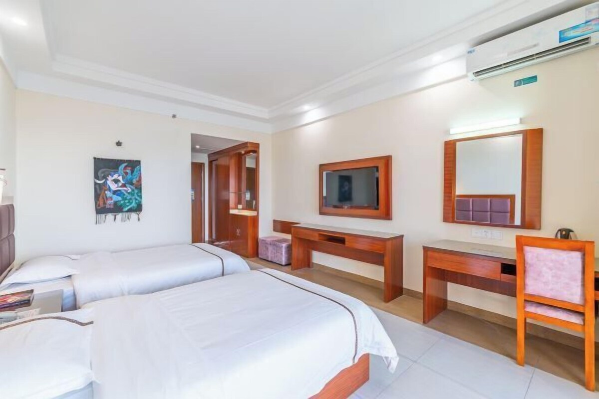A hotel room with two beds, a desk, a chair, a TV, and a large mirror.