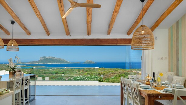 Zona de menjador amb vista al mar, bigues de fusta i llums de vímet penjants.