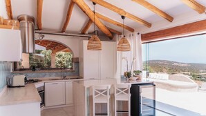 Cuina moderna amb armaris blancs, una illa central i llums penjants de vímet.