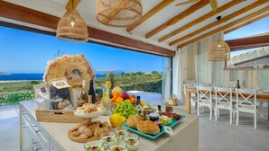 Buffet de desig amb varietat de pastissos, fruites i begudes, davant d'una vista panoràmica de l'oceà.
