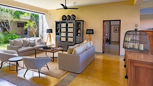 A modern living room with a sofa set, a coffee table, and a cabinet. There is a view of a garden outside. - Taru Villas THE Long House (Bentota)