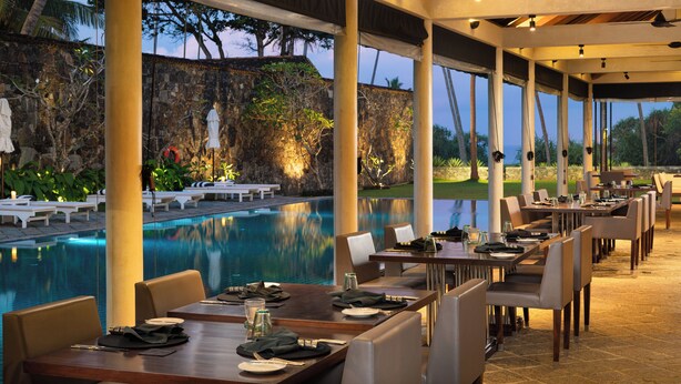 An outdoor dining area with tables and chairs, a pool, and a view of a rocky landscape with trees. - Taru Villas THE Long House (Bentota)