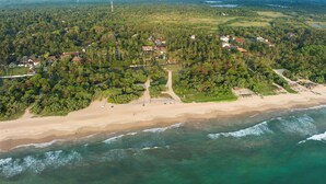 An aerial view of a coastal area with a beach, dense forest, and scattered buildings. - Taru Villas THE Long House (Bentota)