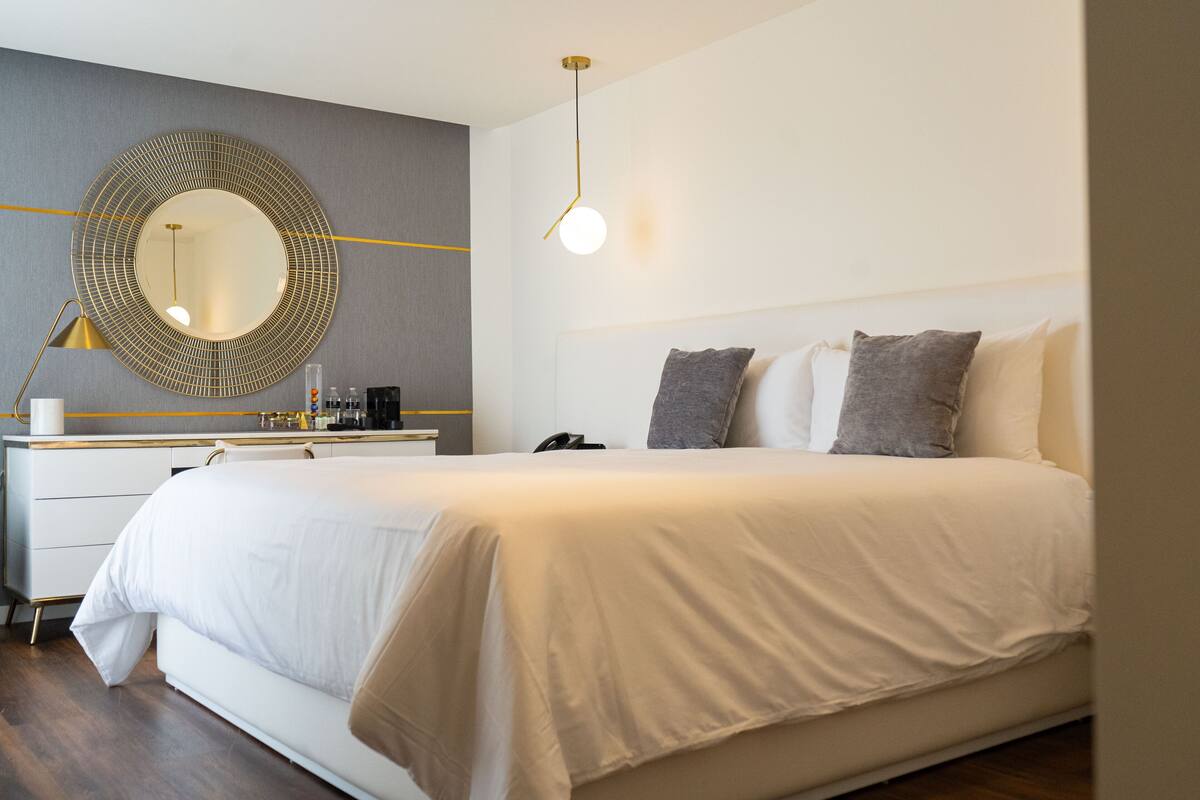 Une chambre d’hôtel moderne avec un grand lit, un miroir rond, une table de chevet et une lampe.