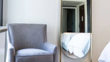 A modern room with a grey armchair, a large mirror, and a bed with white bedding.