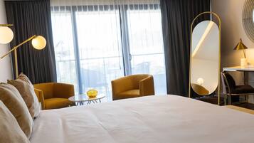 A hotel room with a large bed, two armchairs, a small table, a mirror, and a window with curtains.