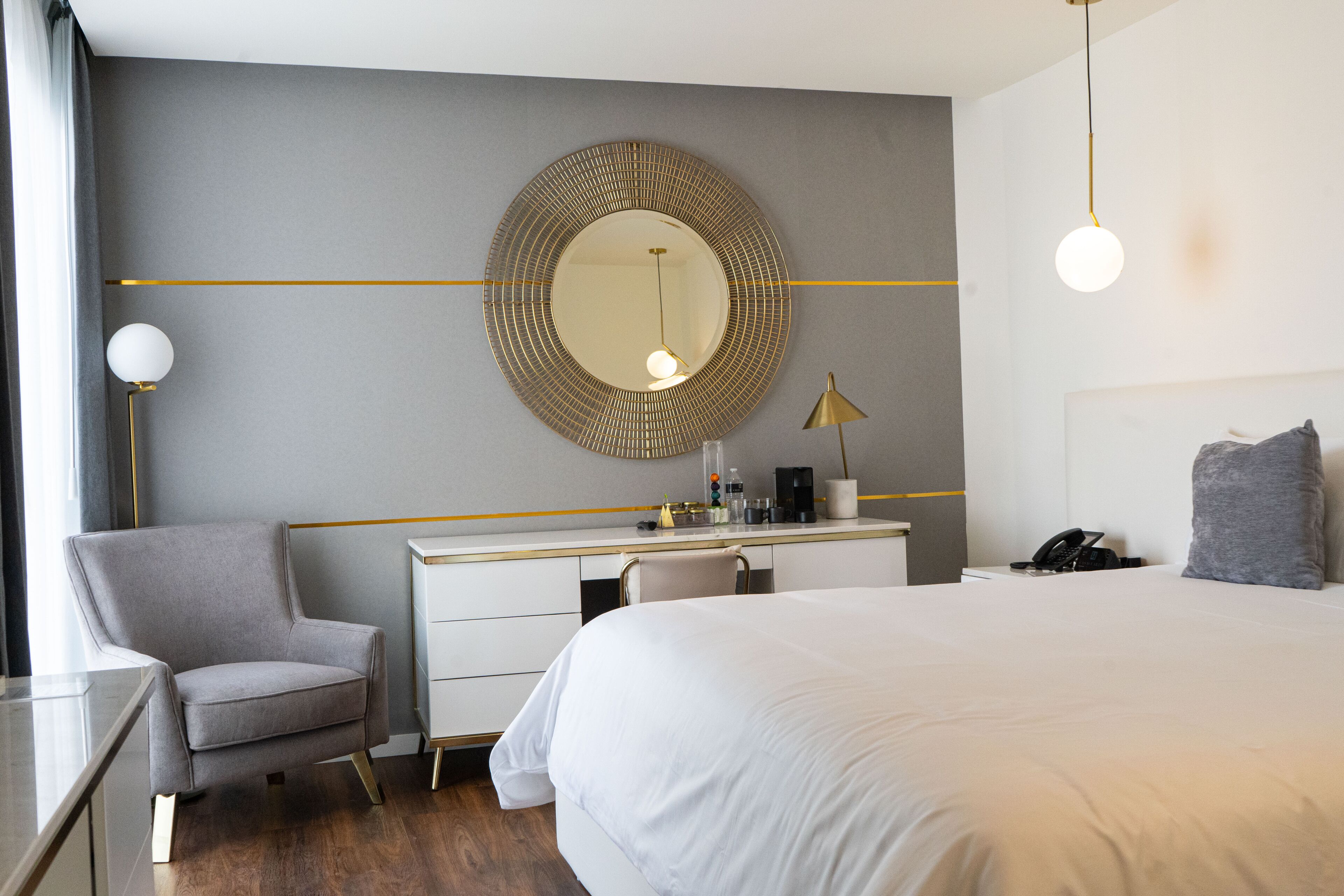 Habitació d'hotel amb un llit, un escriptori amb una cadira, un mirall rodó, una làmpada i un telèfon.