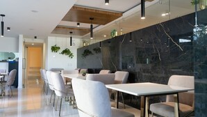 Un comedor moderno con mesas y sillas blancas, un muro decorativo de mármol y plantas colgantes.