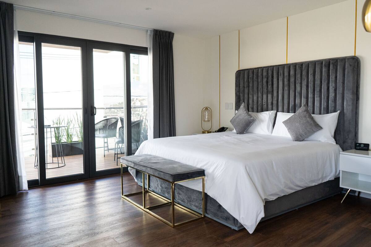 Une chambre à coucher moderne avec un grand lit, un banc, une table de chevet et une vue sur l’extérieur.