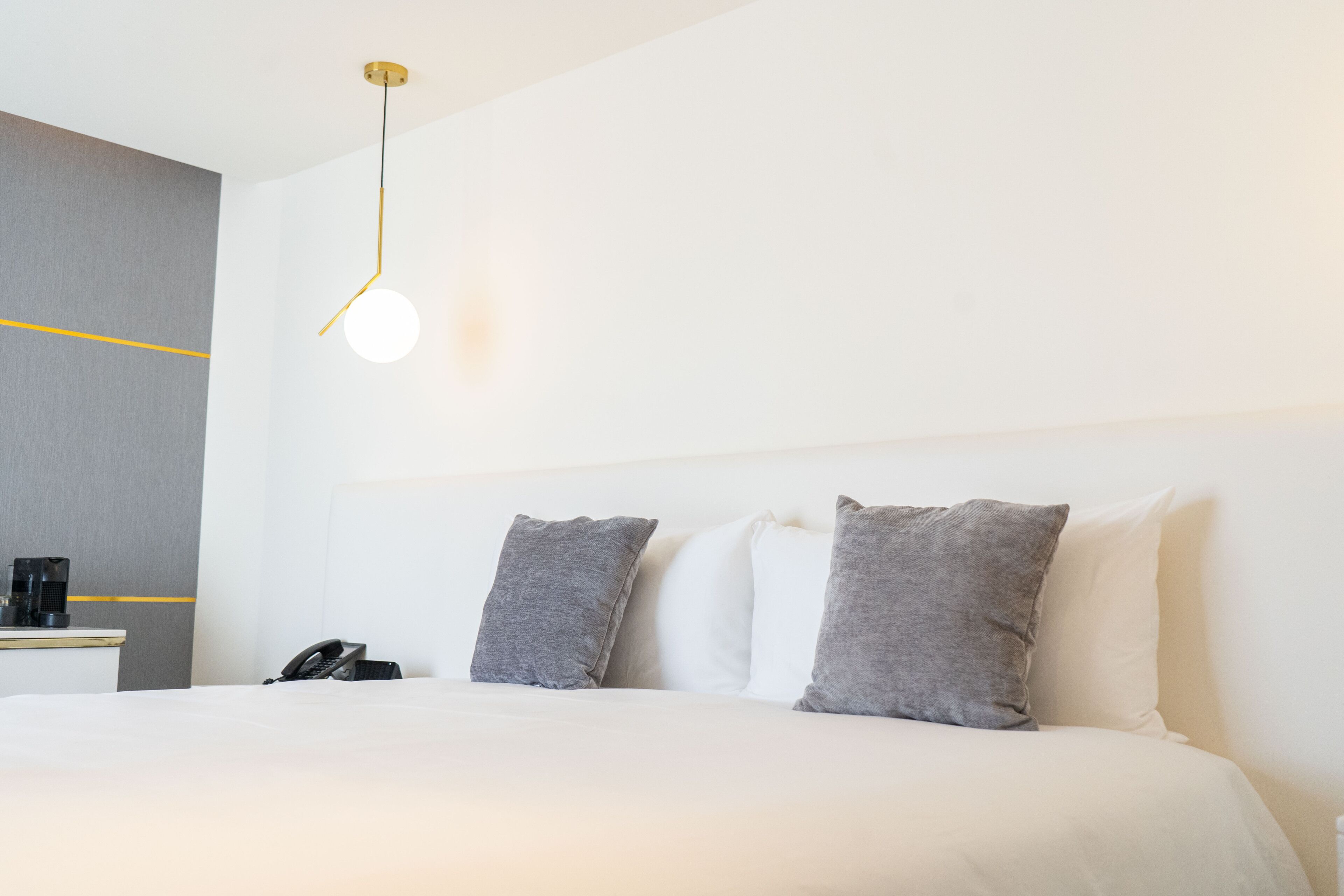 Une chambre d’hôtel comprenant un lit, des oreillers, une table de chevet avec un téléphone et un luminaire fixé au mur.