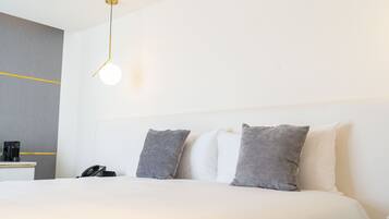 Une chambre d’hôtel comprenant un lit, des oreillers, une table de chevet avec un téléphone et un luminaire fixé au mur.