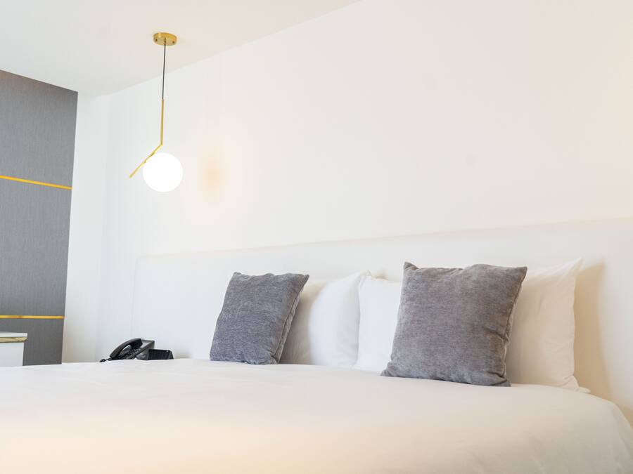 Une chambre d’hôtel comprenant un lit, des oreillers, une table de chevet avec un téléphone et un luminaire fixé au mur.