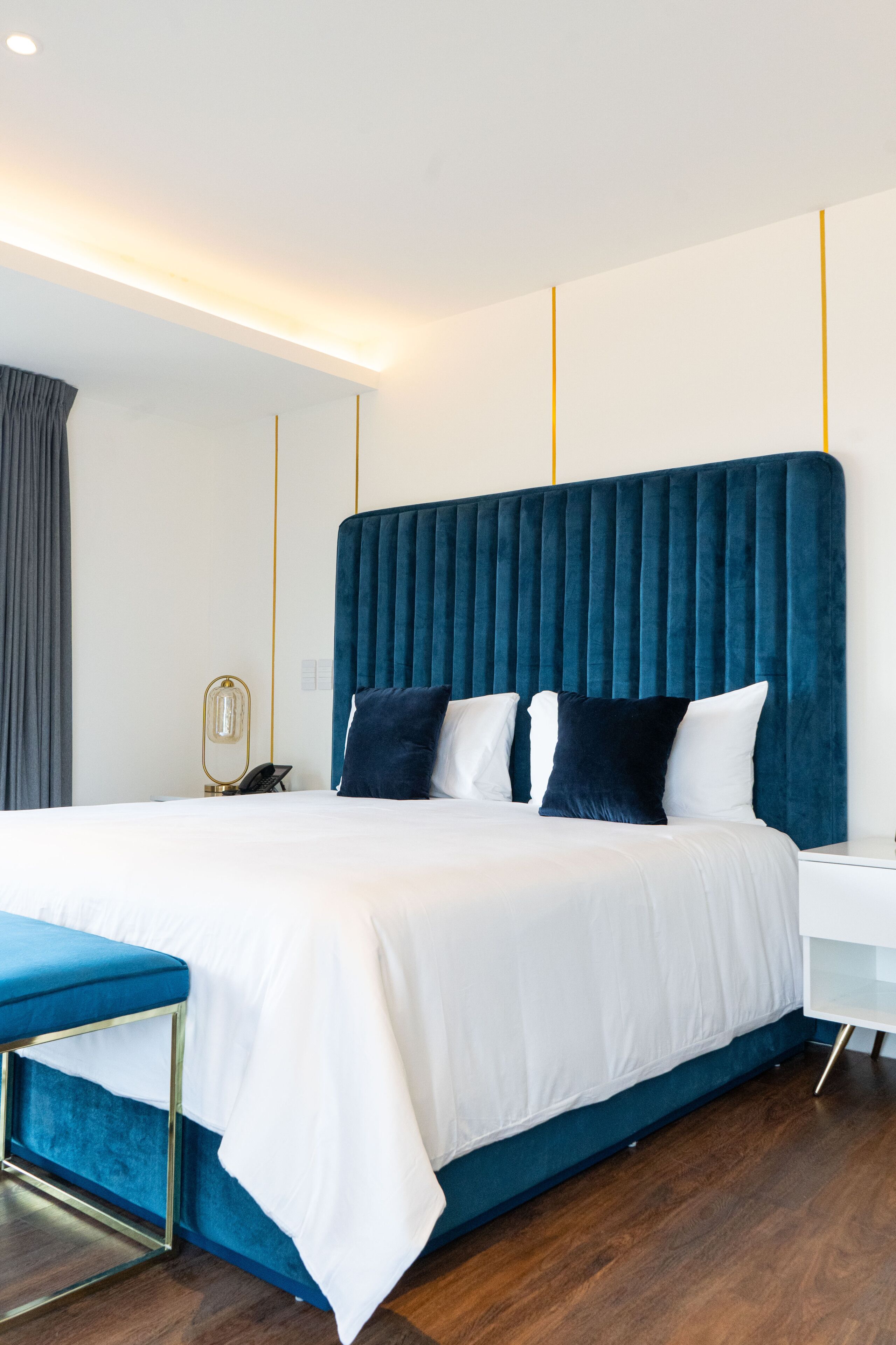 Un dormitorio moderno con una cama grande, una mesita de noche y un banco azul.