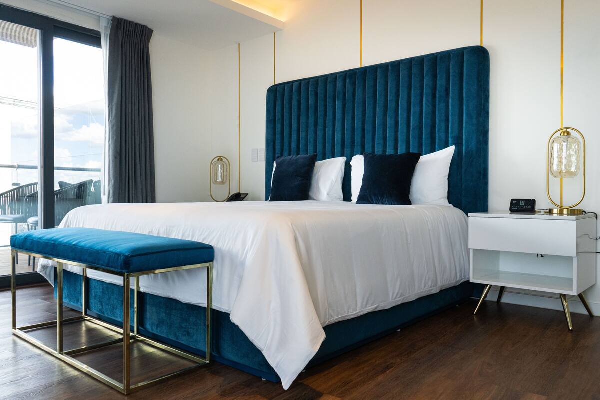 Une chambre d’hôtel moderne avec un grand lit, une banquette, une table de chevet et une vue sur le balcon.
