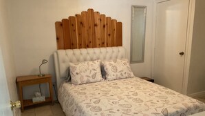 Un dormitori amb un panell de fusta al capçal, una taula de nit amb una làmpada i un llit amb roba de llit estampada.