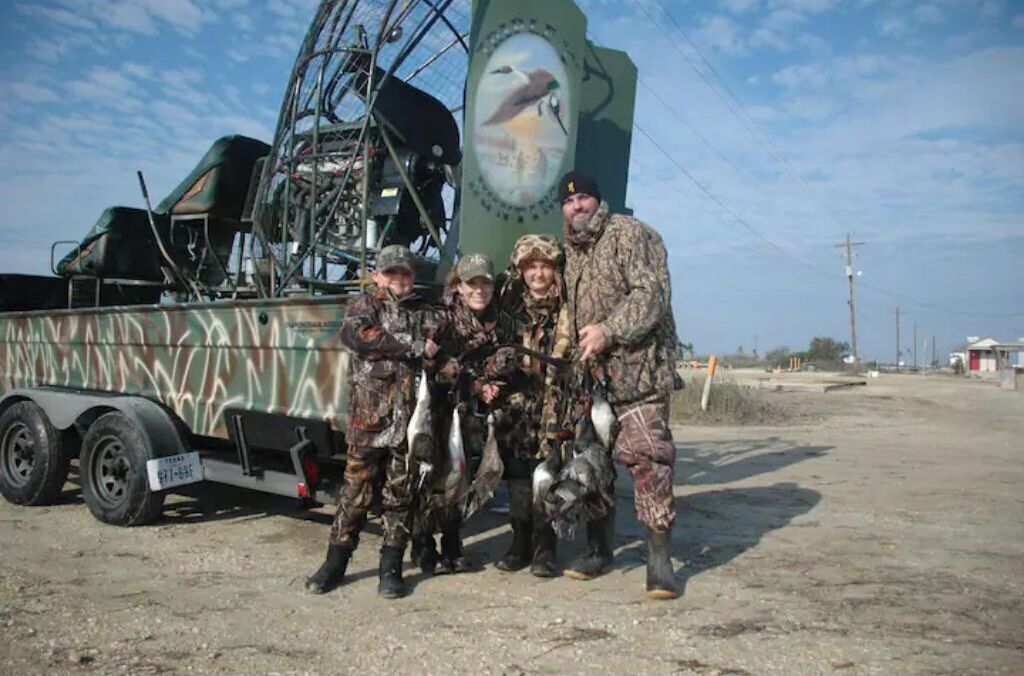 Un grupo de personas vestidas con ropa de camuflaje posando frente a un camión con un gran adhesivo de un ave.